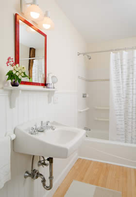 Bathroom with beige walls, white tub and sink, wood floors and red wood vanity mirror with white shelf